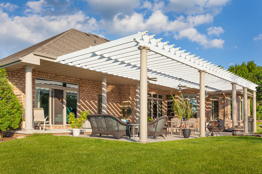 A picture of a luxurious white pergola supported by pillars over a patio seating area for a luxury home.